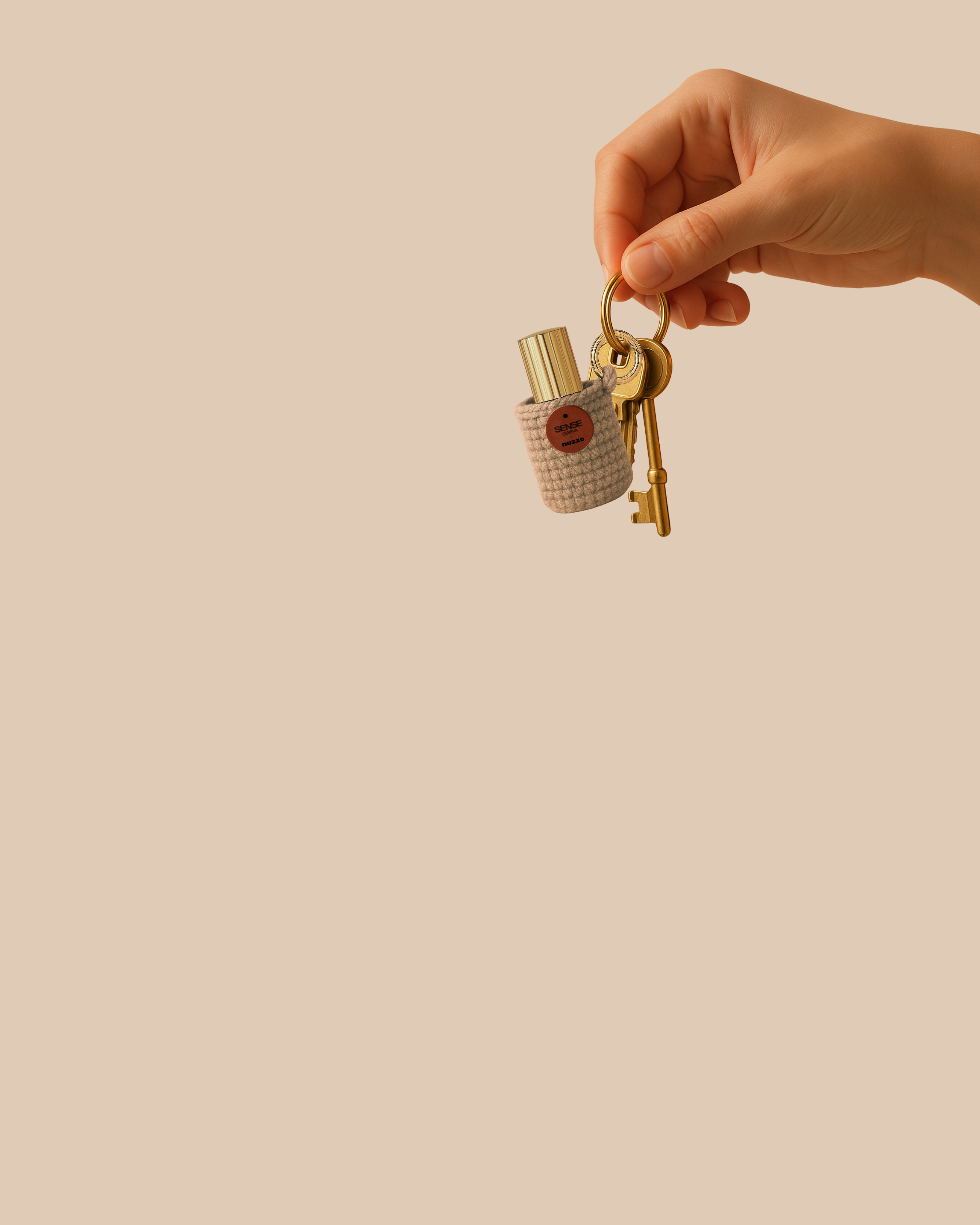 Main tenant un porte-clés doré auquel sont attachées plusieurs clés ainsi qu’un petit étui tricoté beige contenant un flacon de parfum Sense Geneva à capot doré, sur un fond uni couleur sable.