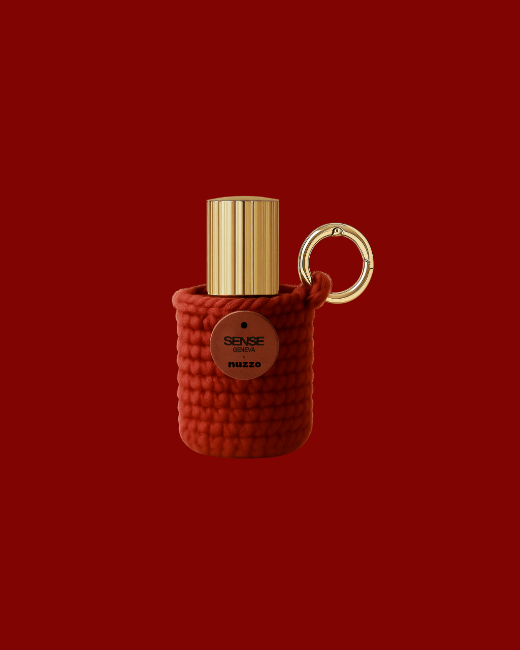Étui porte-parfum Sense Geneva tricoté de couleur rouge brique, contenant un petit flacon à capot doré et accroché à un anneau métallique doré, présenté sur un fond rouge uni.